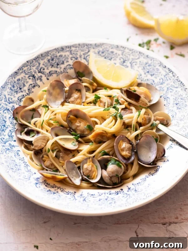 Linguine alle Vongole in a blue bowl with a slice of lemon at the side.