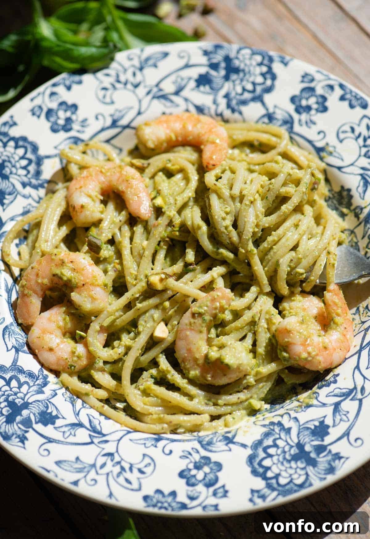 Sicilian Pistachio Pasta with Shrimp and Lemon Cream 4 A side shot of pistachio shrimp spaghetti in a blue bowl sitting on a wooden background.