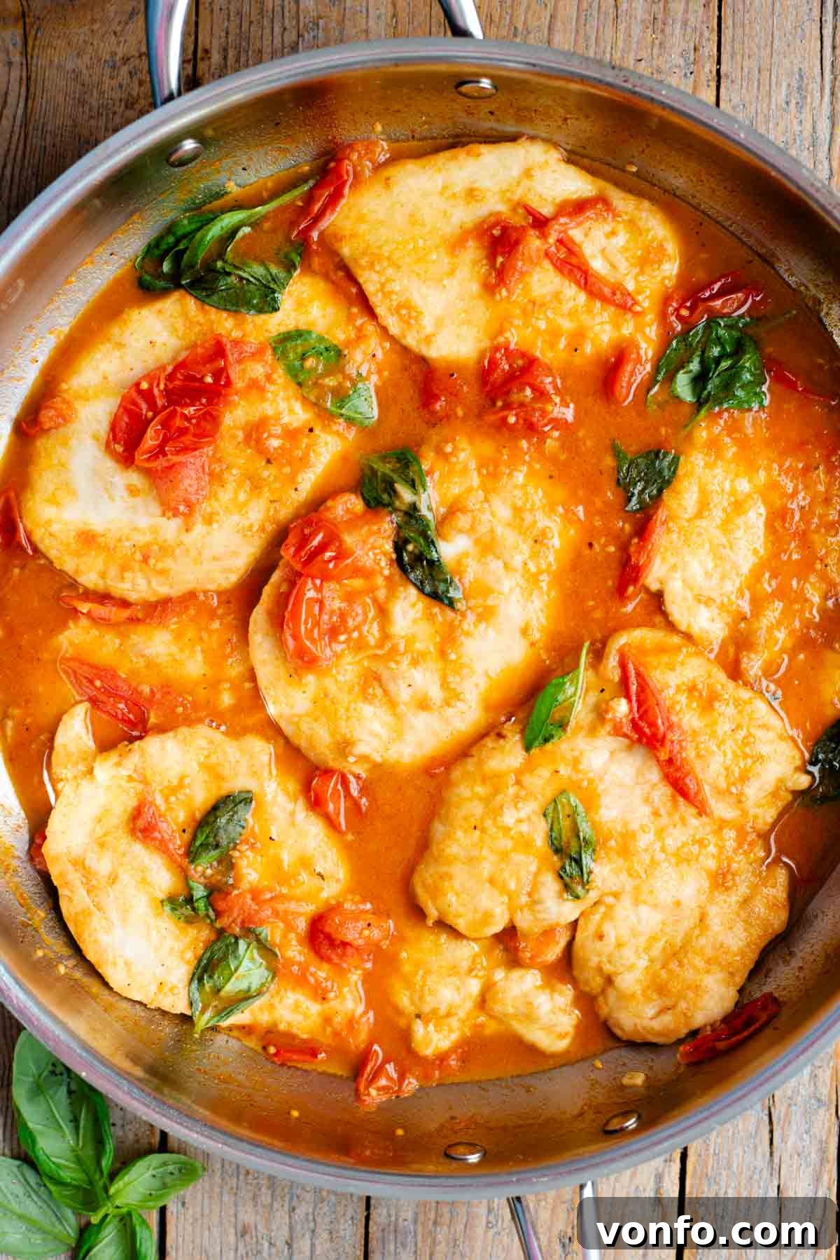 An overhead shot of chicken cutlets in a cherry tomato and basil sauce in a large pan.