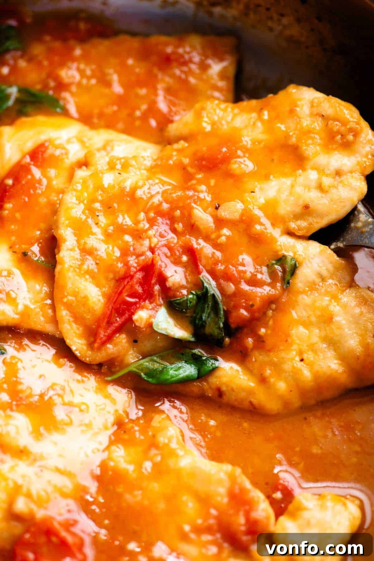 Cherry Tomato Basil Chicken Skillet with Garlic and Parmesan 4 A close up of a piece on chicken in a pan covered in tomato and basil sauce.
