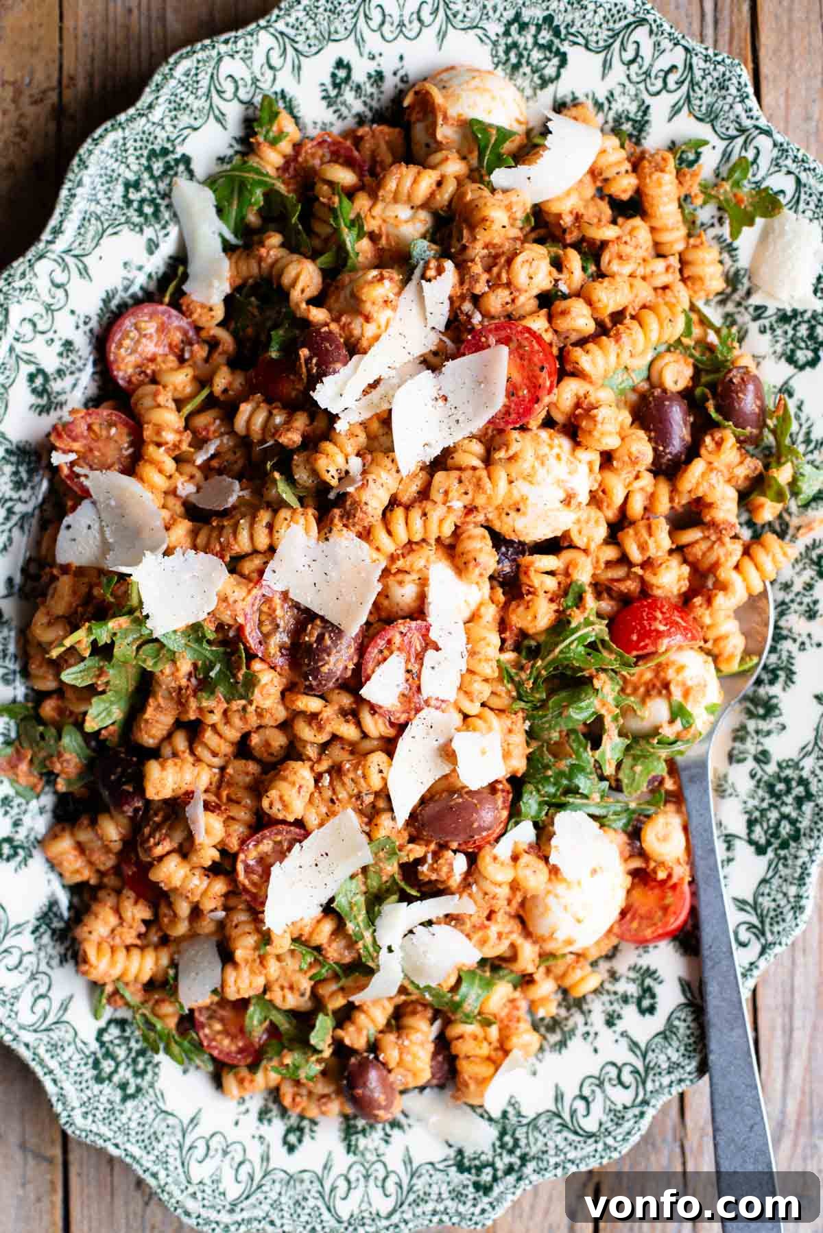 Sun-Dried Tomato Pasta Fredda: Chilled Mediterranean Pasta Salad 2 An overhead shot of a sundried tomato pasta salad on a serving plate with mozzarella, olives, arugula and parmigiano shavings.
