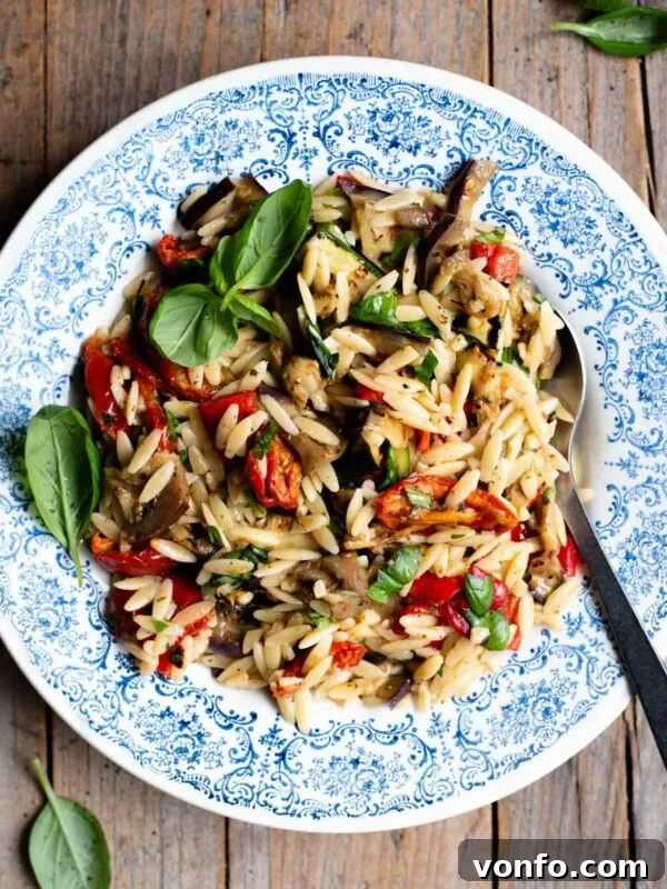Sun-Dried Tomato Pasta Fredda: Chilled Mediterranean Pasta Salad 6 An orzo pasta salad with grilled veg in a blue bowl with a serving spoon at the side. The background is rustic wood.