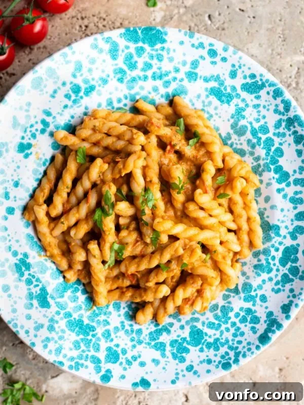 Sun-Dried Tomato Pasta Fredda: Chilled Mediterranean Pasta Salad 7 Pasta in a tuna tomato sauce in a blue and white spotted plate sitting on a travertine surface.