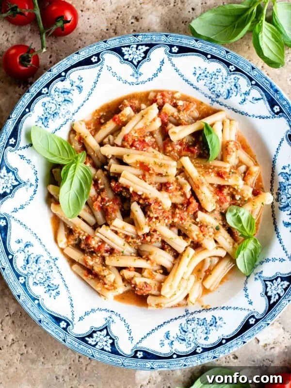 Sun-Dried Tomato Pasta Fredda: Chilled Mediterranean Pasta Salad 8 A blue and white vintage bowl with pasta in a fresh tomato sauce topped with basil. The bowl is on a travertine surface with cherry tomatoes and basil around.
