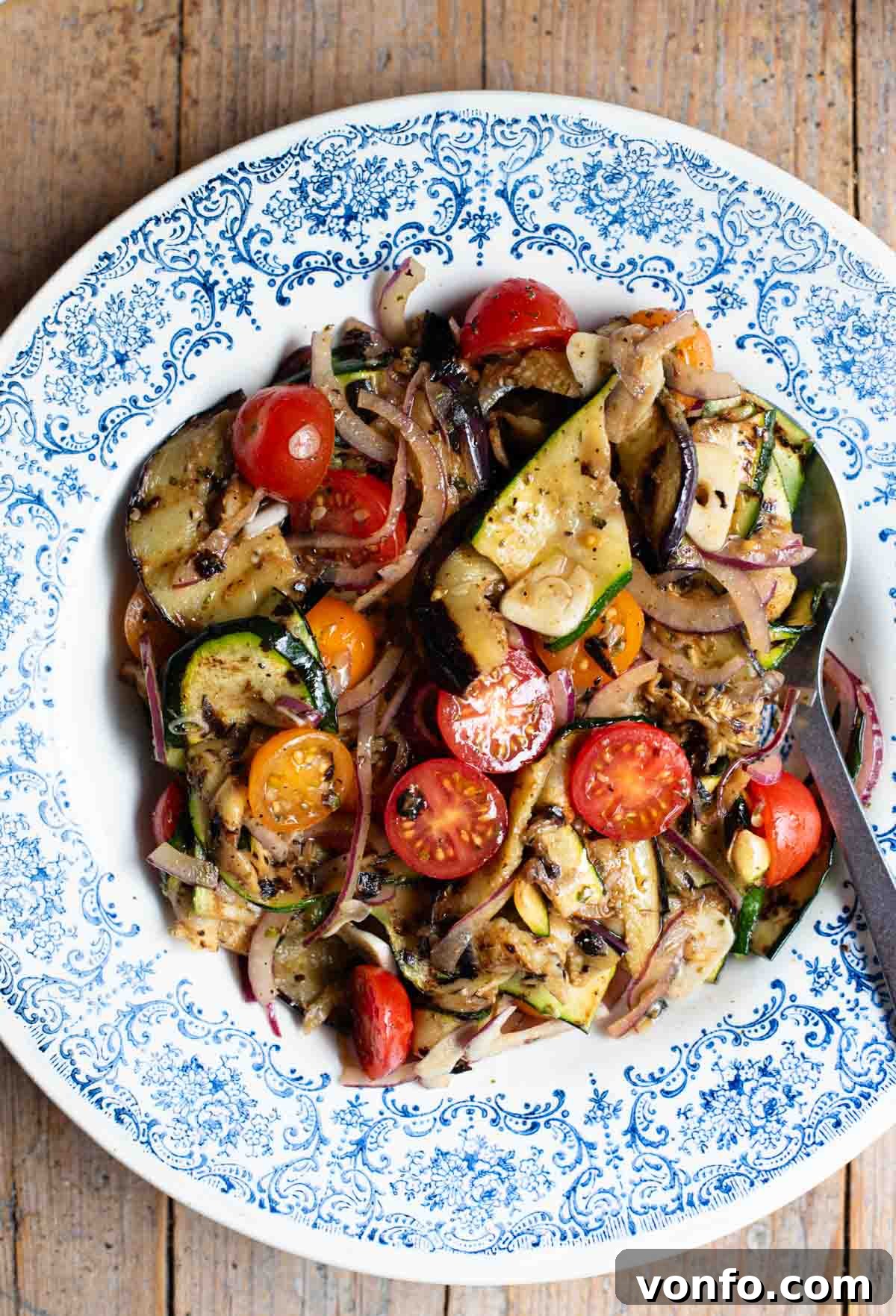 Italian Summer Vegetable Marinade Recipe for Fresh Antipasti 2 An overhead shot of marinated grilled summer vegetables in a blue bowl on a wooden surface.