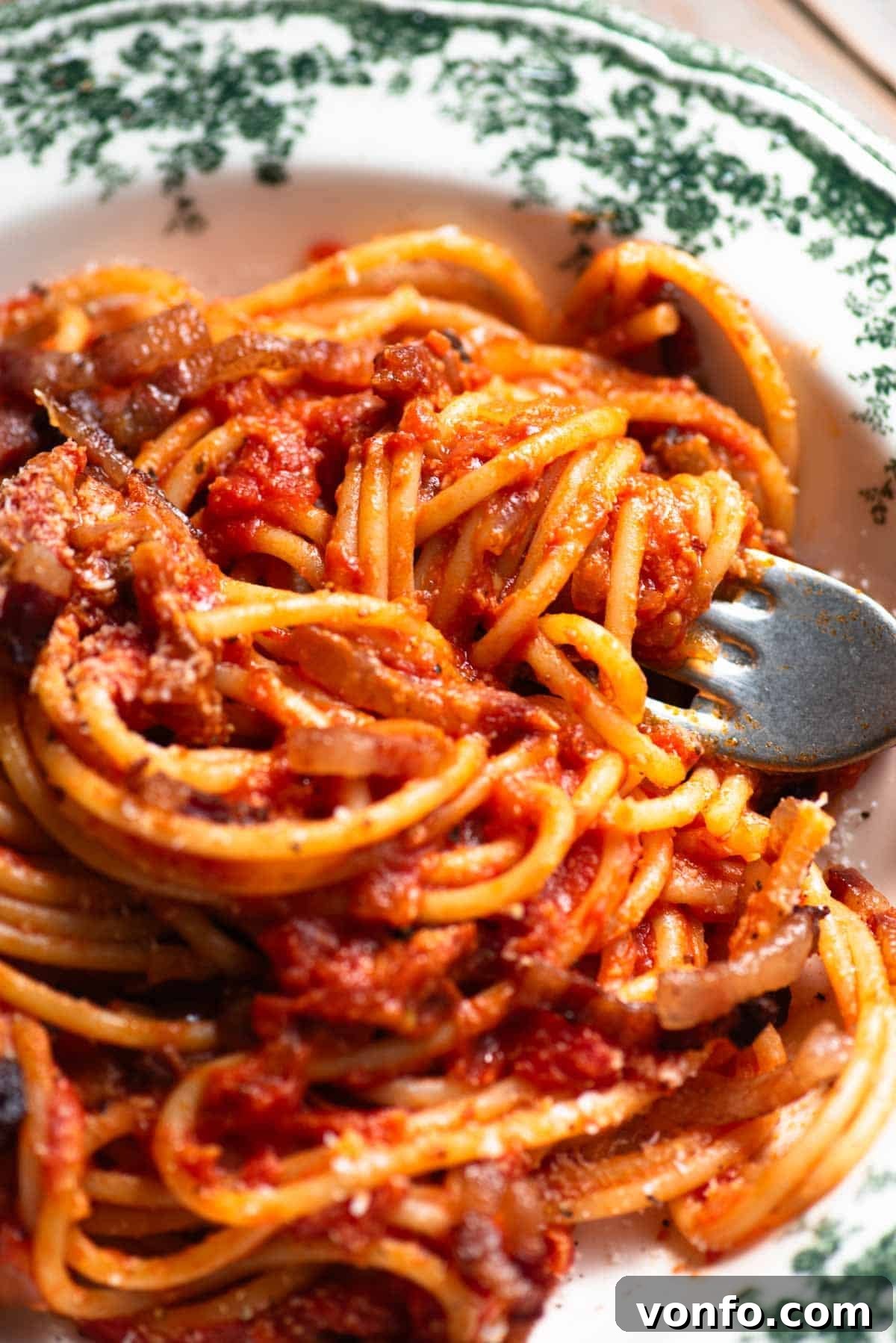 Spaghetti al Rancetto: Umbrian Tomato with Crispy Pancetta 4 A close up of a fork in a bowl with tomato spaghetti topped with pecorino and pancetta.