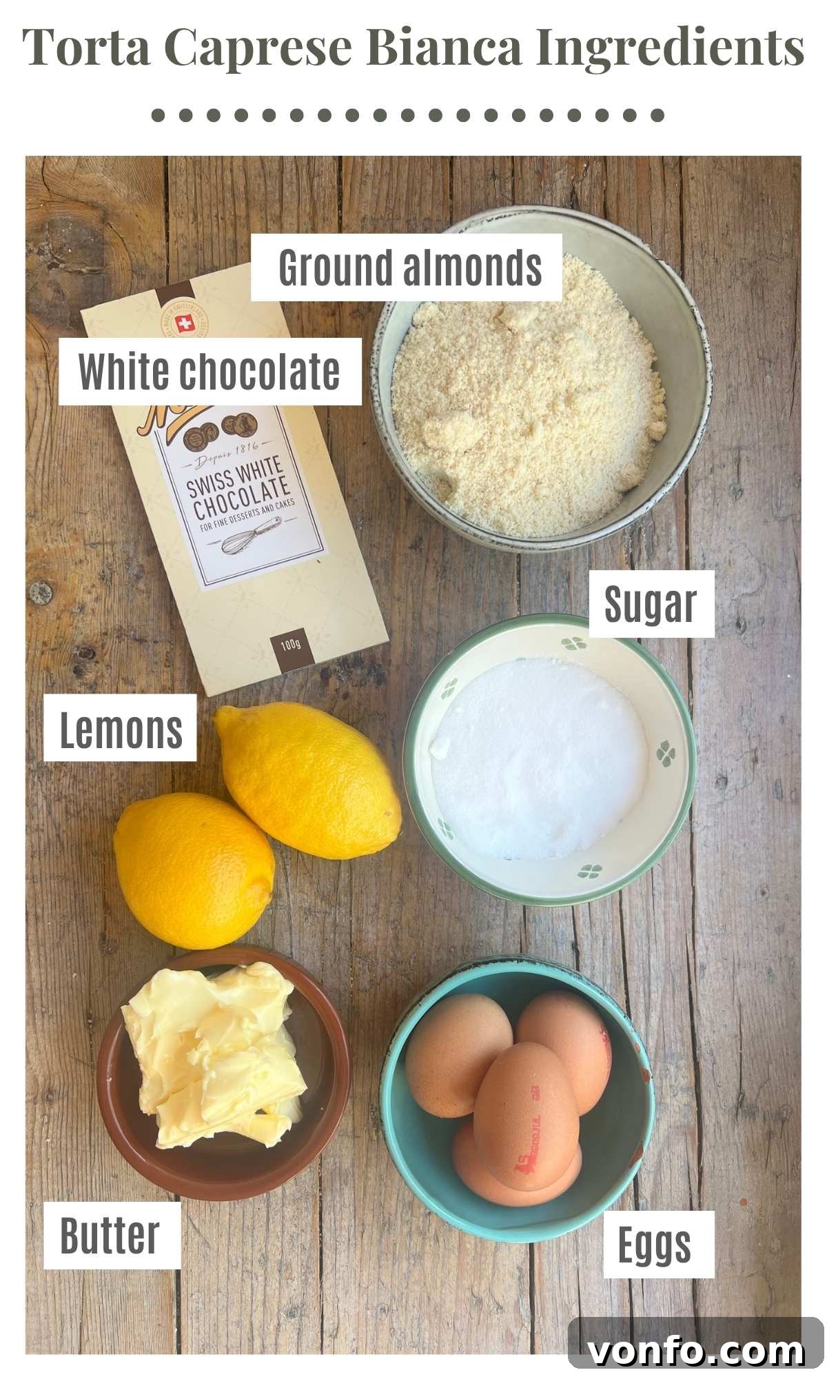 Torta Caprese Bianca: Italian Lemon White Chocolate Cake 3 An overhead shot of all the ingredients needed to make a torta caprese bianca laying out on a rustic wooden surface.
