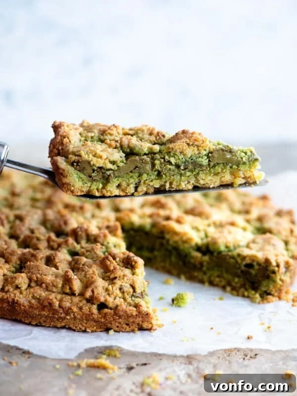 A cake slice holding up a slice of pistachio crumb cake showing a layer of pistachio in the middle.
