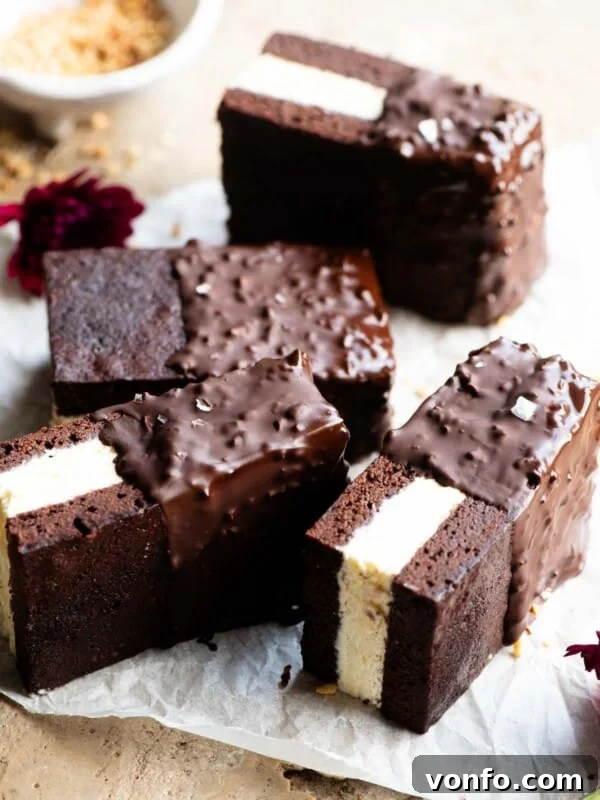 Four chocolate ice cream sandwiches with vanilla ice cream in the middle and dipped in chocolate and hazelnuts on a travertine surface.
