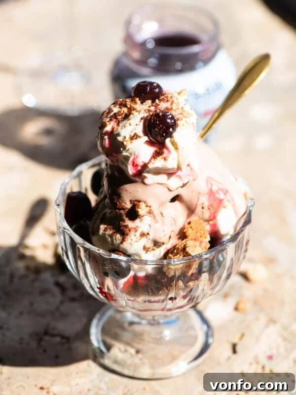 An Italian ice cream sundae in a glass bowl with cream and cherries on top sitting on a travertine surface.