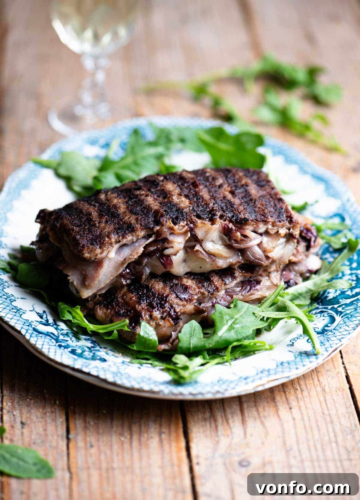 Italian Tramezzino: Beef with Radicchio, Cheese and Porchetta 2 Two slices of stuffed beef stuffed with cheese, radicchio and porchetta on top of each other on a blue plate garnished with arugula.
