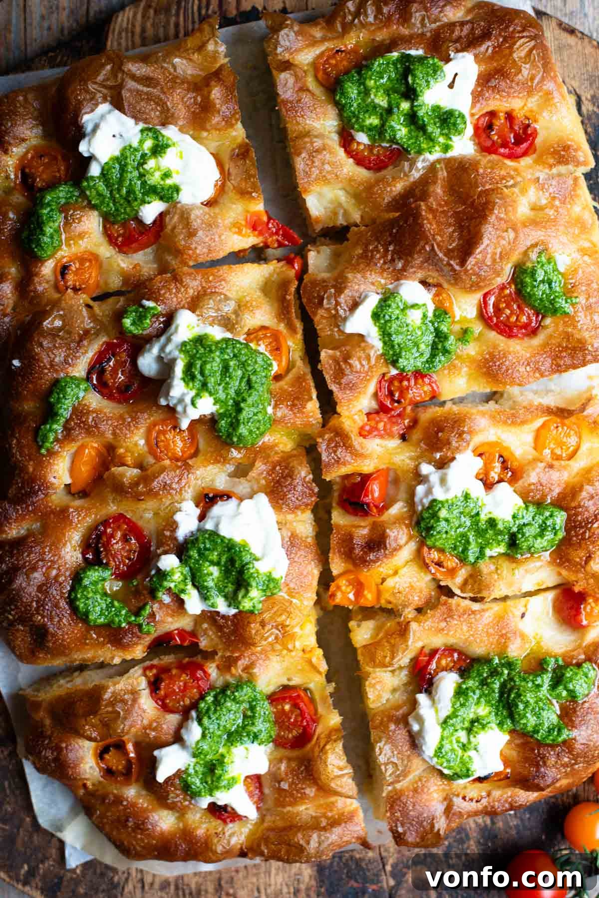 Roasted Tomato Focaccia with Burrata and Basil Pesto 14 An overhead shot of a focaccia cut into 8 slices and topped with cherry tomatoes, pesto and burrata.