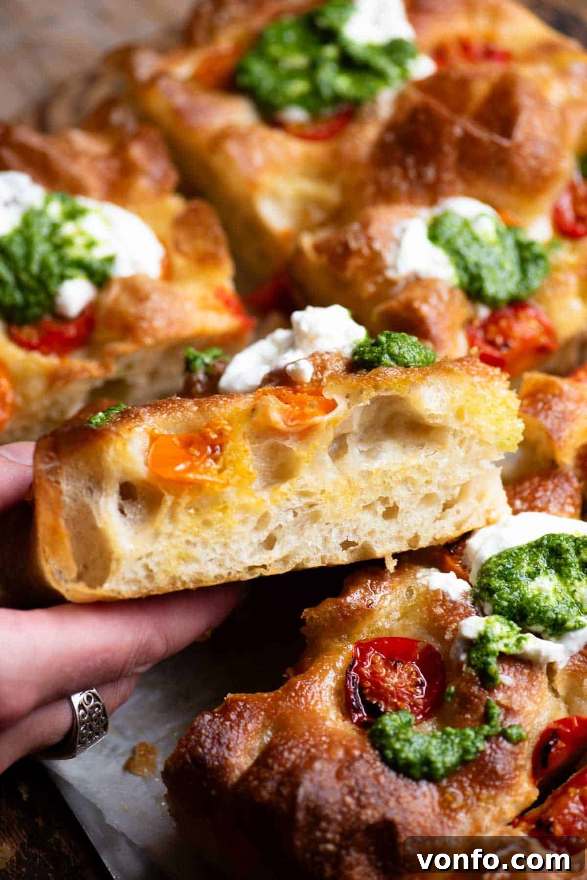 Roasted Tomato Focaccia with Burrata and Basil Pesto 4 A close up of a hand holding a slice of focaccia showing the airy and light texture inside.