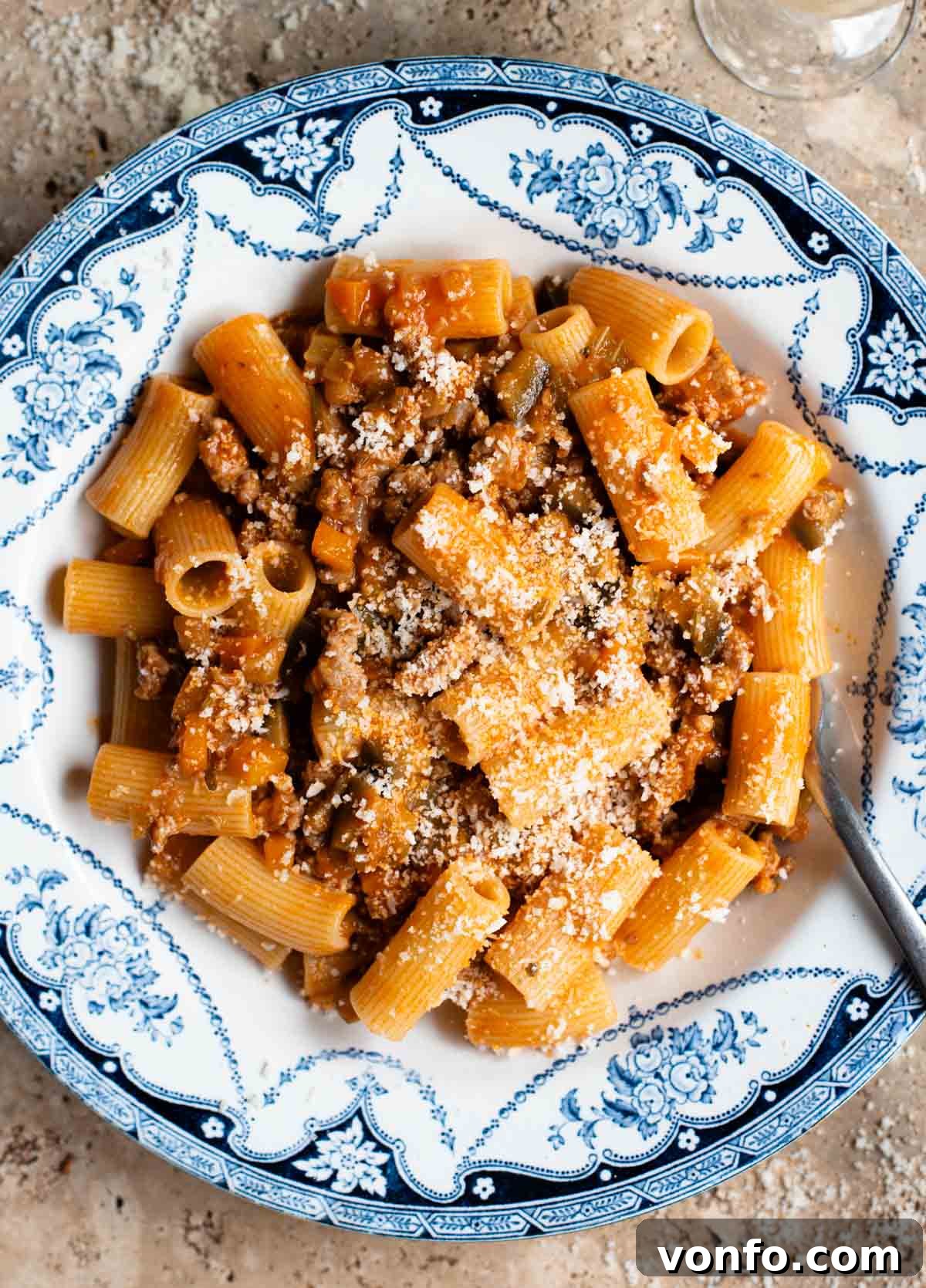Slow-Braised Eggplant and Sausage Ragu 2 An overhead shot of rigatoni pasta with a sausage and eggplant ragu in a blue and white bowl on a travertine surface.