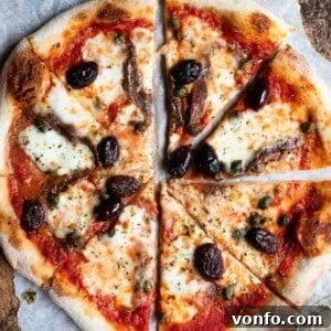 Mediterranean Pizza with Olives, Anchovies & Capers 9 A close up of a pizza cut into slices topped with olives, capers ad anchovies.