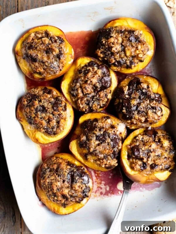 An overhead shot of baked peaches stuffed with amaretti cookies and chocolate in a white baking dish on a rustic wooden background.
