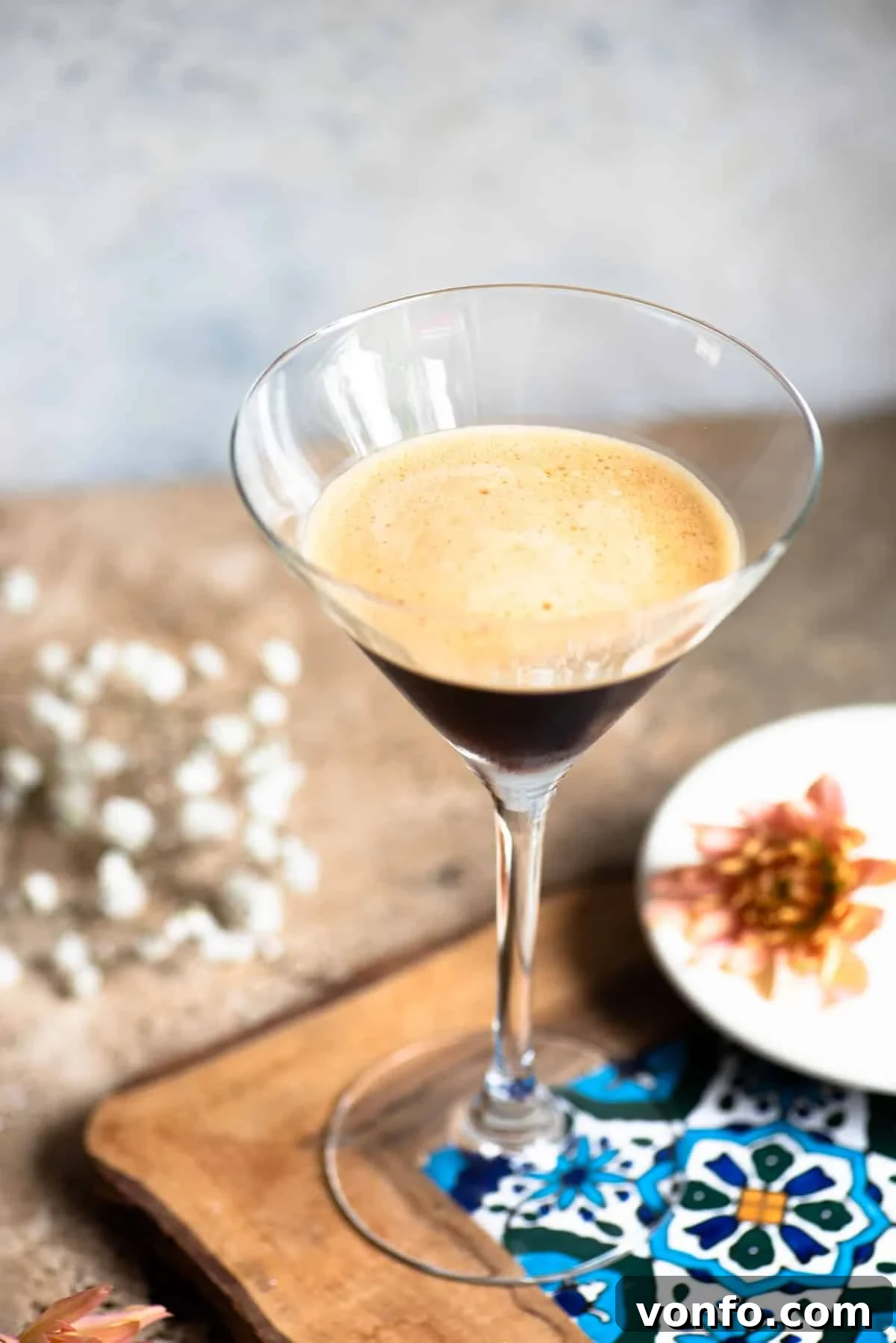A martini glass filled with an iced coffee on a patterned tile with flowers at the side.