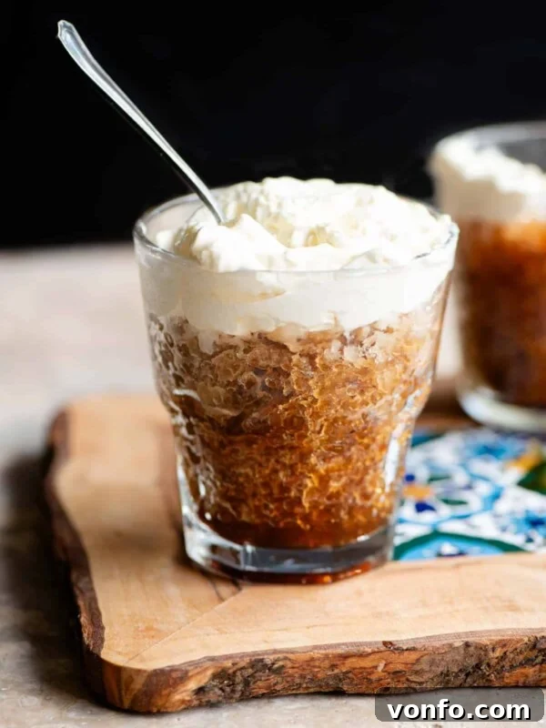 A small glass of coffee granita topped with whipped cream and a spoon in it.