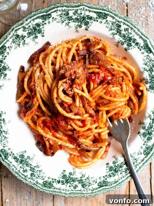 An overhead shot of spaghetti in a green and white vintage style bowl with a tomato and pancetta sauce.