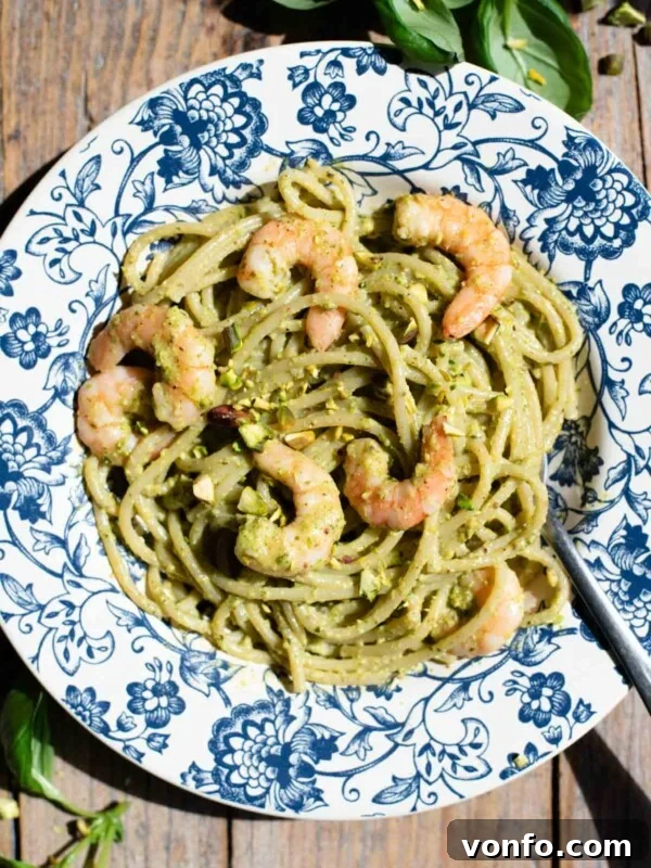 An overhead shot of pistachio pasta with shrimp in a blue floral bowl on a wooden background.
