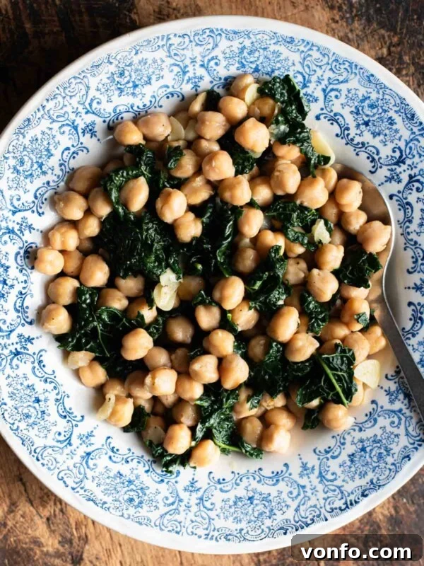 Chickpeas with garlic and cavolo nero in a blue and white bowl sitting on a rustic wooden surface.