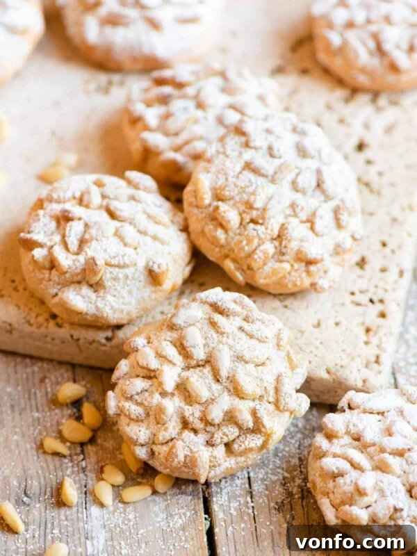 Pignoli cookies on a wooden surface dusted with powdered sugar
