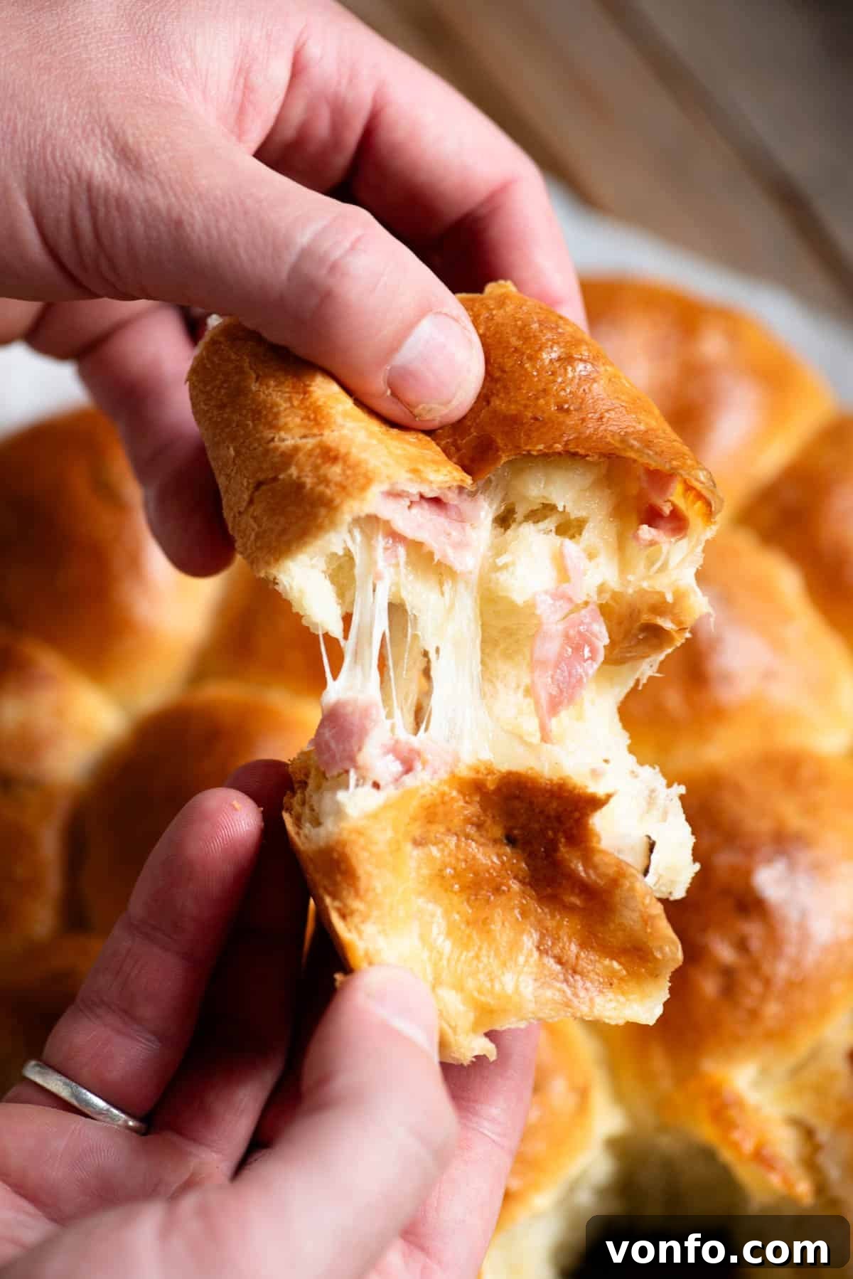 Danubio Salato: Neapolitan Savory Stuffed Brioche Buns 4 A hand tearing open a piece of danubio salato to show the cheese pull and ham inside.